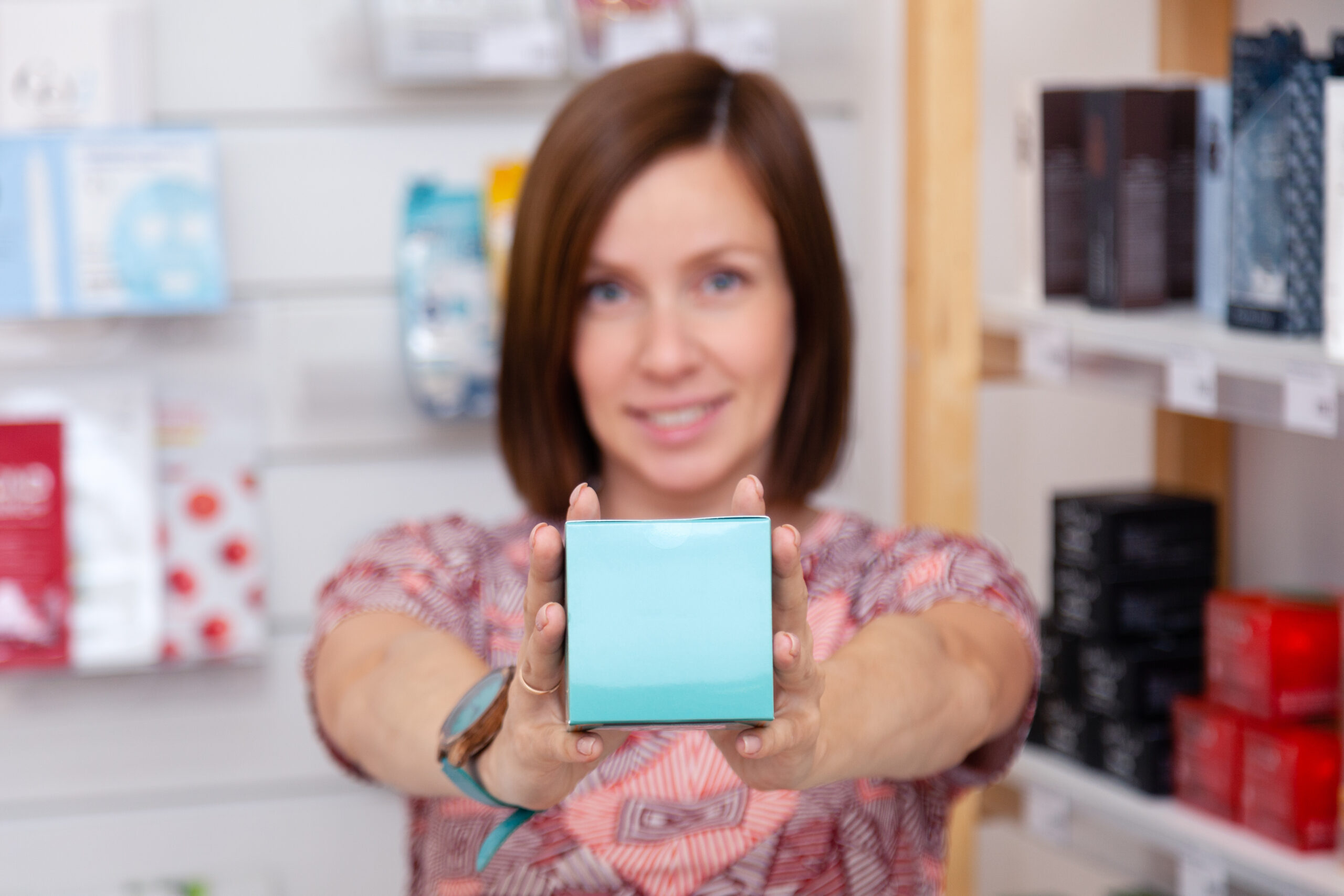 Pretty young pregnant caucasian woman choose skincare product body, face, eyelids, hold box with place for inscription. Cosmetics shop, perfume, medical goods. Pregnancy and shopping. Copyspace