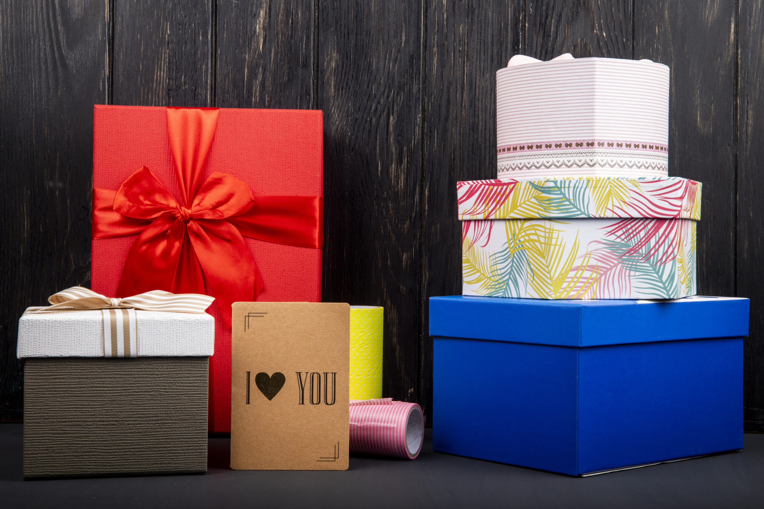 side view of a stack of colorful present boxes and a small i love you card at dark wooden background
