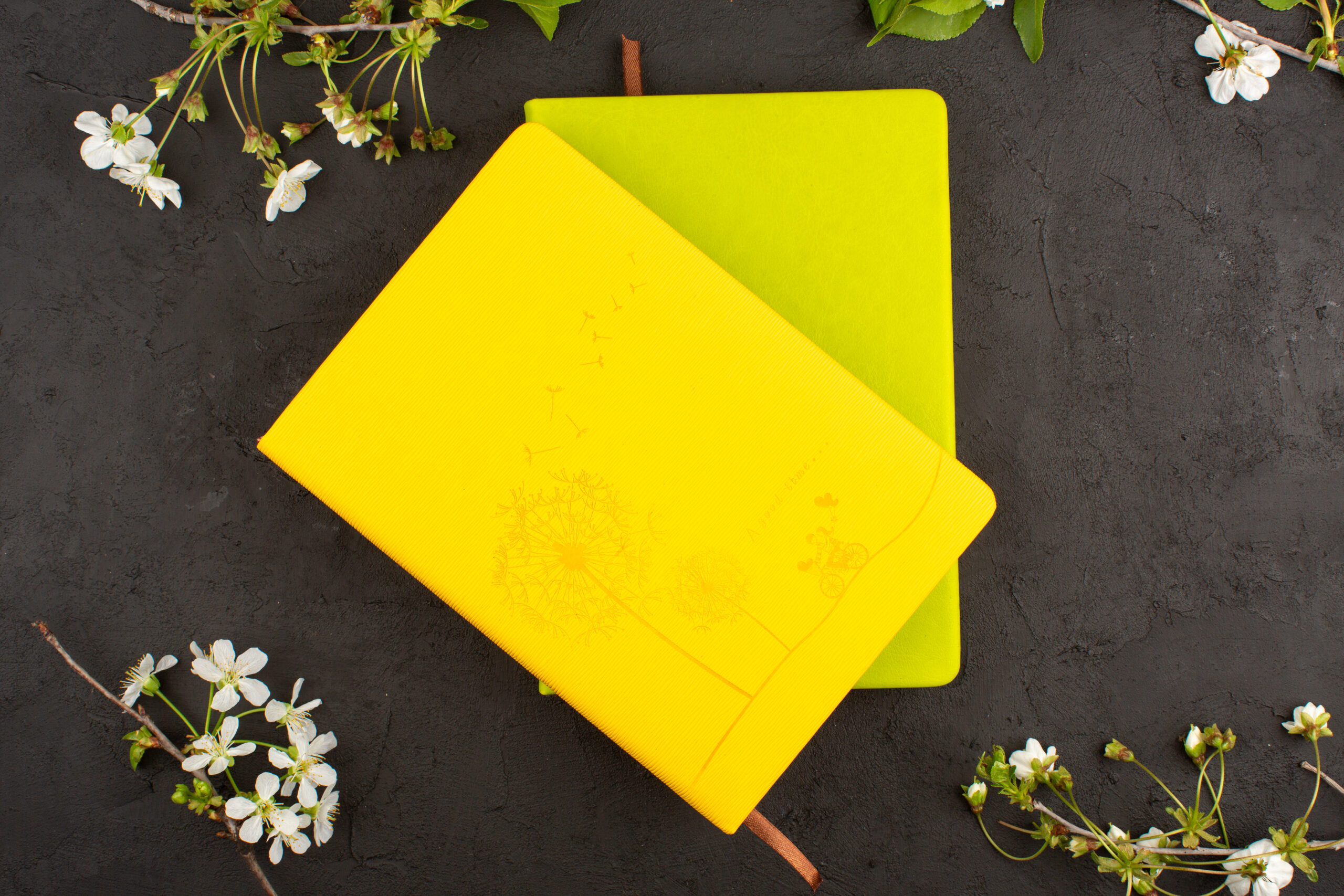 top-view-copybooks-yellow-mustard-colored-around-white-flowers-dark-floor