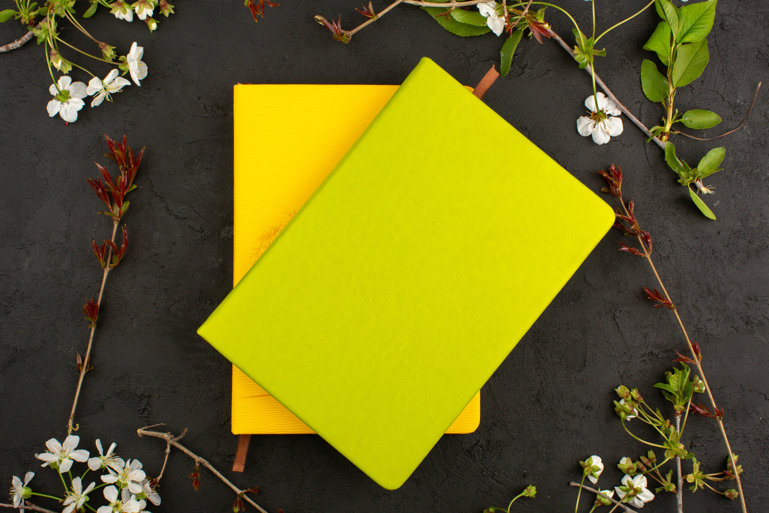 top-view-yellow-copybooks-around-white-flowers-dark-floor