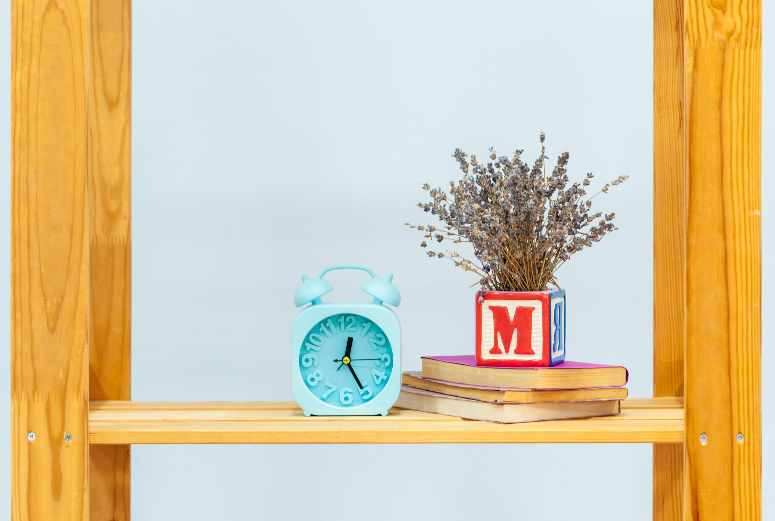 Wooden shelf with alarm clock and objects against blue background